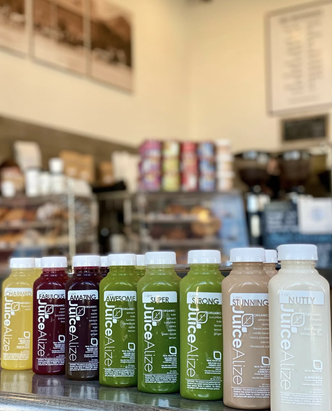 Eight JuiceAlize cold-pressed juice and almond mylk bottles lined up on a counter